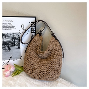 Detailed close-up of woven beige straw hobo bag with brown leather strap and silver buckle