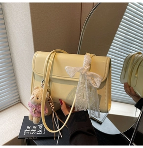 Détail du sac crème avec un nœud en dentelle blanche et un charmant ours en peluche