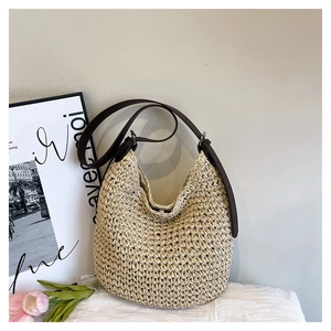 Detail of hand-woven straw bucket bag with adjustable brown leather strap on a soft cushion