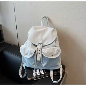 Detail view of a light blue nylon backpack with flap pockets on a leather sofa