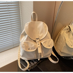 Detail view of cream backpack with front flap pockets and silver metal buckles