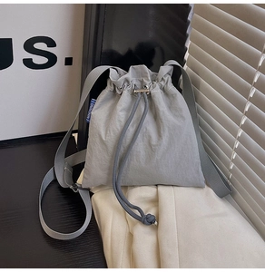 Macro shot of grey drawstring bucket bag with pleated nylon fabric and blue woven brand label