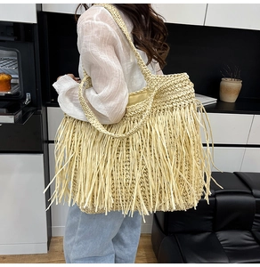 Macro detail of the woven straw tote bag with long hanging fringes and shoulder straps