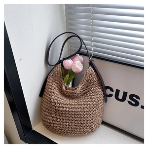 Detailed view of handmade woven straw bucket bag with dark brown leather shoulder strap