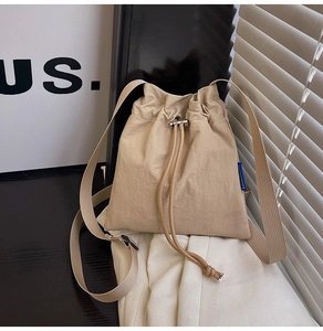 Detail of khaki nylon bucket bag with drawstring closure and blue side label