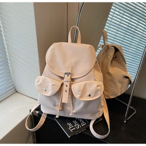 Detail view of a pale nylon backpack featuring twin front pockets and buckle flap design