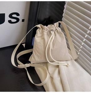Detail view of beige nylon drawstring bucket bag with blue logo tag and shoulder strap