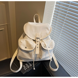 Detail view of cream nylon backpack featuring leather buckle and two front magnetic pockets