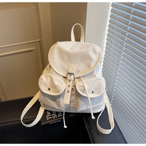 Detail view of white minimalist backpack featuring multiple front pockets and flap closure