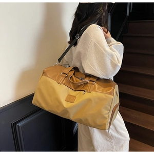 Large travel tote bag with brown and yellow color blocking shown on woman's shoulder