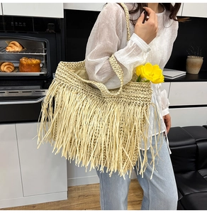 Detailed view of beige straw tote bag featuring long bohemian tassels and shoulder strap