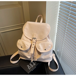 Close-up of cream canvas backpack with flap buckle closure and dual front utility pockets