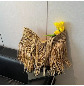 Detailed close-up of handmade straw tote bag featuring long bohemian style tassels