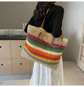 Close-up of a large rainbow striped woven straw tote bag with brown leather handles