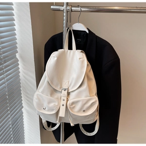 Detail view of cream-colored faux leather backpack with flap buckle and twin front pockets
