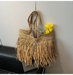 Detailed texture of straw woven tote bag featuring long bohemian tassels and handles