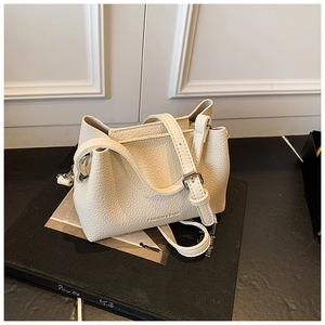 Détail d'un sac seau en cuir litchi blanc cassé montrant la texture et la boucle réglable