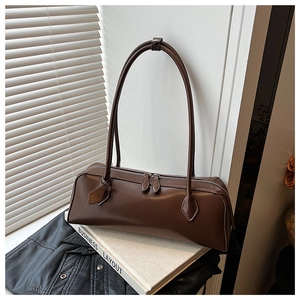 Close-up of brown faux leather baguette bag with dual zippers on a white display box