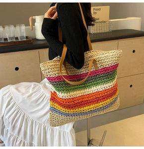 Detail shot of a large rainbow woven straw tote bag featuring brown leather shoulder straps