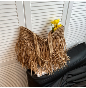 Detailed view of a woven straw tote bag with long fringe on a stylish leather sofa