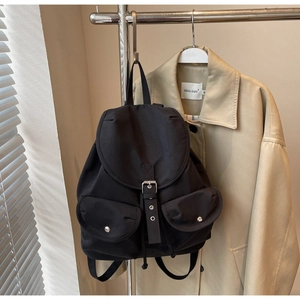 Detail of a black nylon backpack with silver buckles hanging next to a trench coat