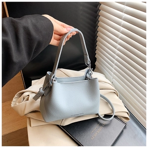 Détail du sac seau bleu clair avec motif litchi, logo et finitions métalliques chic