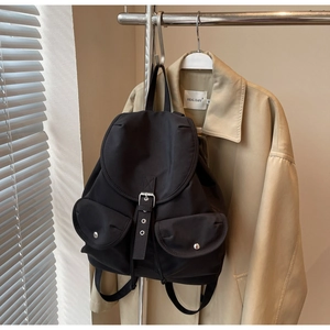 Close-up of black canvas backpack with flap cover and silver metal buckles against a trench coat