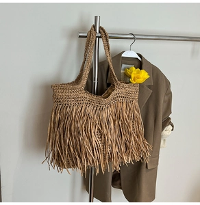 Detail of hand-woven straw tote bag with fringes hanging on a minimalist hanger