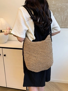 Women's handmade straw bucket bag with dark brown strap in a minimalist home setting
