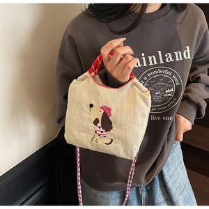 Detail of embroidered dachshund pattern on a cream canvas crossbody bag with red straps