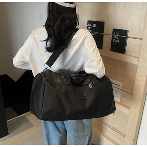 Large black travel bag with wide adjustable strap shown in a minimalist lifestyle setting