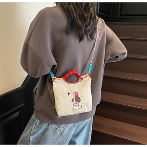 Detail of canvas crossbody bag with cartoon dog embroidery and colorful woven rope straps