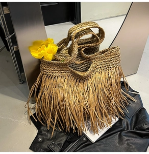 Detail of bohemian straw woven tote bag featuring dense fringe tassels and textured finish