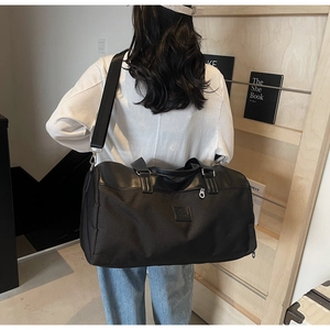 Detail of a large black nylon travel bag featuring leather handles and adjustable shoulder strap