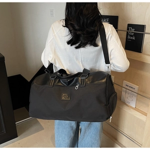 Black canvas travel bag with leather trim shown on model against a bookshelf background