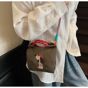 Detail view of brown crossbody bag with cartoon dog embroidery and colorful woven ropes