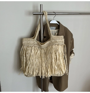 Detail of bohemian straw tote bag featuring long decorative tassels and woven handles