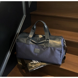 Detail of navy canvas travel bag with leather logo and sturdy adjustable shoulder strap