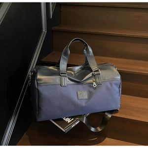 Close-up of navy canvas duffle bag with black leather accents and silver hardware