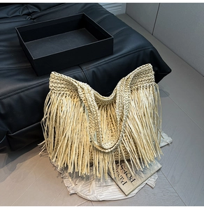 Detailed close-up of a large beige straw tote bag featuring long fringe and woven texture