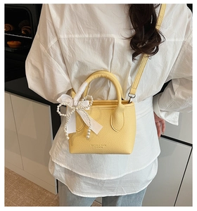Detail of yellow lychee leather mini bucket bag with pearl charm and white satin bow decoration