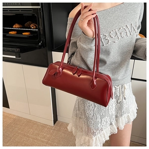 Detail of red cylindrical baguette bag with smooth finish and dual handles on shoulder