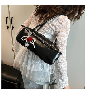 Detail of black glossy leather shoulder bag with red heart and pearl pendant charm