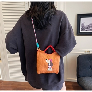 Detail of orange dachshund embroidered bag with colorful woven strap and red handle