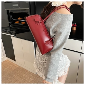 Close-up of deep red glossy cylindrical shoulder bag with elegant minimalist strap