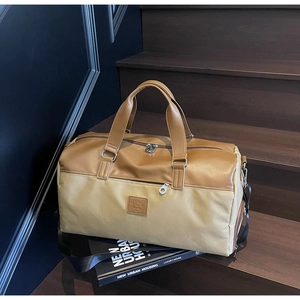 Detail of a large capacity travel bag in khaki canvas and brown leather on wooden stairs