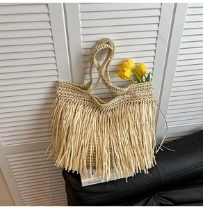Detail of hand-woven beige straw tote bag featuring long decorative fringe and top handles