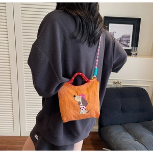 Close-up of orange dog-patterned crossbody bag with colorful woven shoulder strap