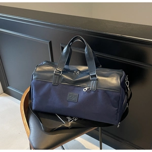 Detail of navy canvas travel bag featuring leather patchwork and dual zippers on a chair