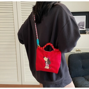 Detail of red canvas crossbody bag featuring dog embroidery and colorful woven strap